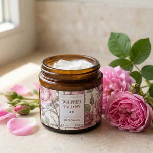 Könnte beinhalten: Ein braunes Glas mit weißer geschlagener Talgcreme, beschriftet mit "Whipped Tallow" und "Damascus Rose 100% Natural". Rosa Rosenblüten und -blüten umgeben das Glas. Das Glas enthält 125 ml Produkt.
