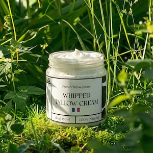 May include: A clear glass jar filled with white whipped tallow cream, set against a backdrop of green grass and foliage. The label reads "French Tallow Cream" and "Whipped Tallow Cream". The jar contains 5 oz / 150ml of 100% natural cream.