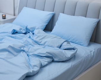 Könnte beinhalten: Ein weißes Bettgestell mit einem hellblauen Bettbezug und zwei hellblauen Kissen. Das Bett steht vor einer weißen Marmorwand.