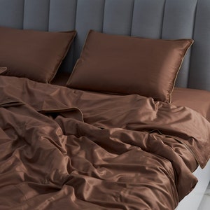 May include: A brown duvet cover with a subtle sheen, folded on a bed with two matching brown pillows. The bed has a gray headboard with vertical panels.