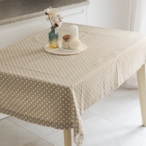 May include: A beige tablecloth with white polka dots, featuring a decorative centrepiece with a vase of cotton stems, a candle, and a seashell.