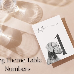 May include: A white card with the word "table" written in cursive and the number "1" in black. A black and white illustration of a dog's head is to the left of the number. The card is on a light brown surface.