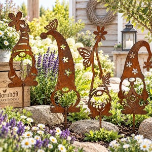 May include: Four rust-colored metal garden stakes shaped like gnomes with tall, pointed hats. Each gnome features cut-out details including flowers and butterflies. The stakes are positioned upright in a garden bed with green plants and flowers.