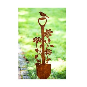 Op de afbeelding: Een roestige metalen tuindecoratie in de vorm van een schop met een vogel die bovenop zit en bloemen die langs de steel groeien.