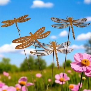 Op de afbeelding: Vier metalen tuinpalen in de vorm van libellen, met een roestbruine afwerking. De libellen hebben gedetailleerde vleugelontwerpen en zijn geplaatst in een tuin met roze bloemen en een blauwe lucht op de achtergrond. Deze decoratieve palen voegen een speels tintje toe.