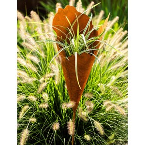 Pode incluir: Um vaso de metal enferrujado em forma de cone com uma planta verde dentro. O vaso está rodeado de grama verde.