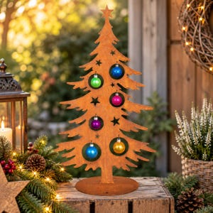 Peut inclure: Une silhouette de sapin de Noël en métal couleur rouille avec une étoile au sommet et des découpes pour suspendre des ornements. L'arbre est décoré de six petites boules brillantes et multicolores : bleu, vert, magenta, violet et doré.