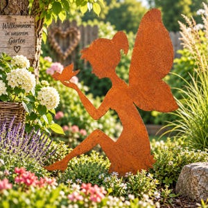 Könnte beinhalten: Eine rostfarbene Metall-Gartenfigur einer sitzenden Fee mit Flügeln, die einen kleinen Vogel in einer Hand hält. Die Silhouette zeigt eine Figur mit Pferdeschwanz, platziert inmitten von grünem Blattwerk und Blumen im Garten.