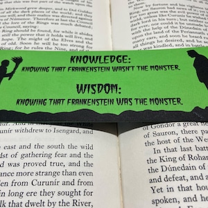 May include: A green bookmark with black text and silhouettes of two figures. The text reads "Knowledge: Knowing that Frankenstein wasn't the monster. Wisdom: Knowing that Frankenstein was the monster."