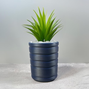 May include: A blue ceramic planter with a ribbed texture, filled with white decorative stones and a green succulent plant.