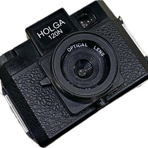 Puede incluir: Una cámara Holga 120N negra con una lente negra y una superficie texturizada.
