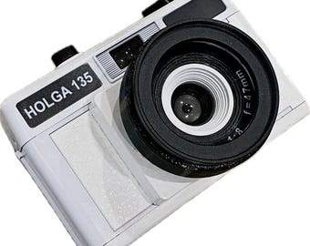 Pode incluir: Uma câmera Holga 135 de plástico branco com uma lente preta. A lente tem um anel branco ao redor da borda com o texto "1:8 F=47mm".