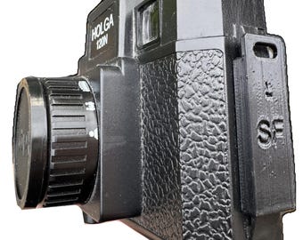 以下が含まれることがあります： 側面にテクスチャ加工されたグリップ、黒いキャップ付きのレンズ、右側にLとSFの文字がサンセリフ体で垂直にエンボス加工された長方形のアタッチメントを備えた、黒いHolga 120Nフィルムカメラ。