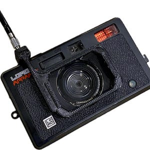 May include: A black Lomography  "Apparat" camera with a red and black lens cover. The camera has a black strap attached to it.