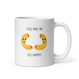 Op de afbeelding: Witte keramische mok met een grappige uitspraak "You Mac Me So Happy!" met twee macaroni-noedels met smiley-gezichten.