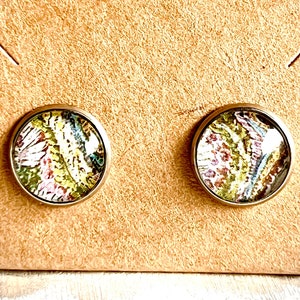 May include: A pair of round, gold-toned earrings with a colorful, abstract pattern inside. The pattern features shades of pink, green, yellow, and brown.
