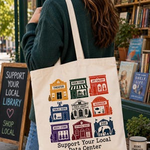May include: A cream-colored canvas tote bag featuring a grid of nine colorful illustrations of local buildings, including a theater, bookstore, art gallery, radio station, library, aquarium, music store, historical society, and zoo, with the text Support Your Local Data Center.