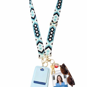 May include: A lanyard with a geometric pattern in teal, black, and white, holding a light blue phone case, keys, sunglasses, and a staff ID badge. The lanyard has a navy blue strap and gold-colored hardware.
