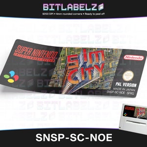 May include: A Super Nintendo Entertainment System game cartridge label for SimCity. The label is black with a colorful image of a city skyline. The text "PAL VERSION" and "MADE IN JAPAN" are printed on the label. The cartridge is for the Super Nintendo Entertainment System.