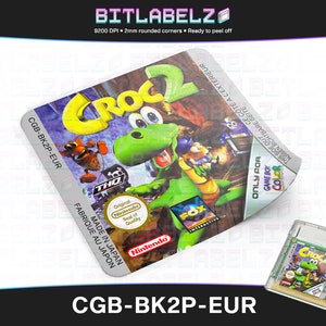 Puede incluir: Un cartucho de juego Game Boy Color para Croc 2, con un personaje de cocodrilo verde sobre un fondo azul y morado. El cartucho está etiquetado como "CGB-BK2P-EUR" y tiene los logotipos de Nintendo y Fox Interactive.