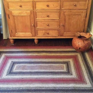 Peut inclure: Un meuble en bois avec plusieurs tiroirs et deux portes se trouve devant un tapis tressé à rayures rouges, brunes et blanches. Un pot en bois se trouve sur le tapis à droite du meuble.