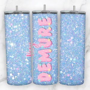 May include: A glittery blue tumbler with the word "DEMURE" in pink bubble letters. The word "Very" is written in pink cursive. The tumbler has a silver lid and is covered in sparkling glitter.