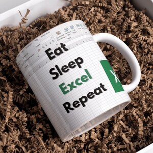 May include: White coffee mug with a green and black design. The mug has a spreadsheet pattern and the text "Eat Sleep Excel Repeat".