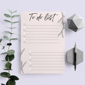 Może przedstawiać: Drukowalna lista rzeczy do zrobienia z jasnoróżowym tłem i czarnymi liniami. Tekst "To do list" jest napisany czarnym kursywą u góry strony. Po lewej i prawej stronie strony znajdują się małe serduszka i wzory kwiatowe.