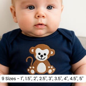 May include: A navy blue baby bodysuit featuring an embroidered brown monkey with white accents. The bodysuit has short sleeves and a round neckline. The text at the bottom reads "9 Sizes - 1", 1.5", 2", 2.5", 3", 3.5", 4", 4.5", 5""