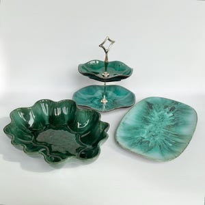 Peut inclure: Un ensemble de trois pièces en céramique avec un vernis vert émeraude et bleu sarcelle profond à la finition brillante. Le lot comprend un présentoir à deux niveaux avec une poignée en métal argenté, un grand bol festonné et un plat rectangulaire.