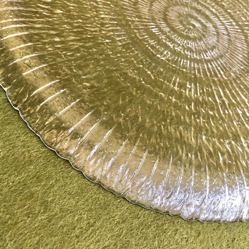 May include: A clear glass plate with a textured, rippled surface. The plate has a circular shape and a raised center.