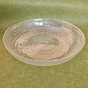 May include: A clear glass serving bowl with a textured, rippled surface. The bowl has a circular shape and a wide, shallow rim.