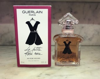 May include: A pink box with the text "GUERLAIN PARIS" and a black and white illustration of a little black dress. The text "La petite Robe noire MA ROBE VELOURS EAU DE PARFUM 30 ml 1.0 FL. OZ" is printed on the box. A clear glass bottle of perfume with a silver cap and a black and white illustration of a little black dress on the front. The text "La petite Robe noire" is printed on the bottle.