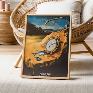 Może przedstawiać: Wydruk w ramie obrazu Salvadora Dalí "Trwałość pamięci", przedstawiającego topiący się zegarek kieszonkowy w surrealistycznym krajobrazie. Wydruk jest umieszczony na białym dywanie przed wiklinowym krzesłem.