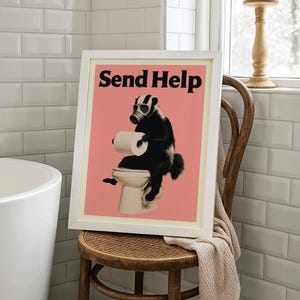May include: Framed art print featuring a badger wearing a gas mask and sitting on a toilet, holding toilet paper. The print has a pink background with the words "Send Help" in black. The artwork is displayed on a wooden chair.