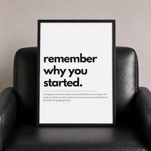 Könnte beinhalten: Ein gerahmter Druck mit den Worten "remember why you started" in fetter schwarzer Schrift. Darunter steht in kleinerem Text: "On tough days...Keep pushing forward." Der Druck befindet sich in einem schwarzen Rahmen, vor weißem Hintergrund, auf einem schwarzen Ledersessel.
