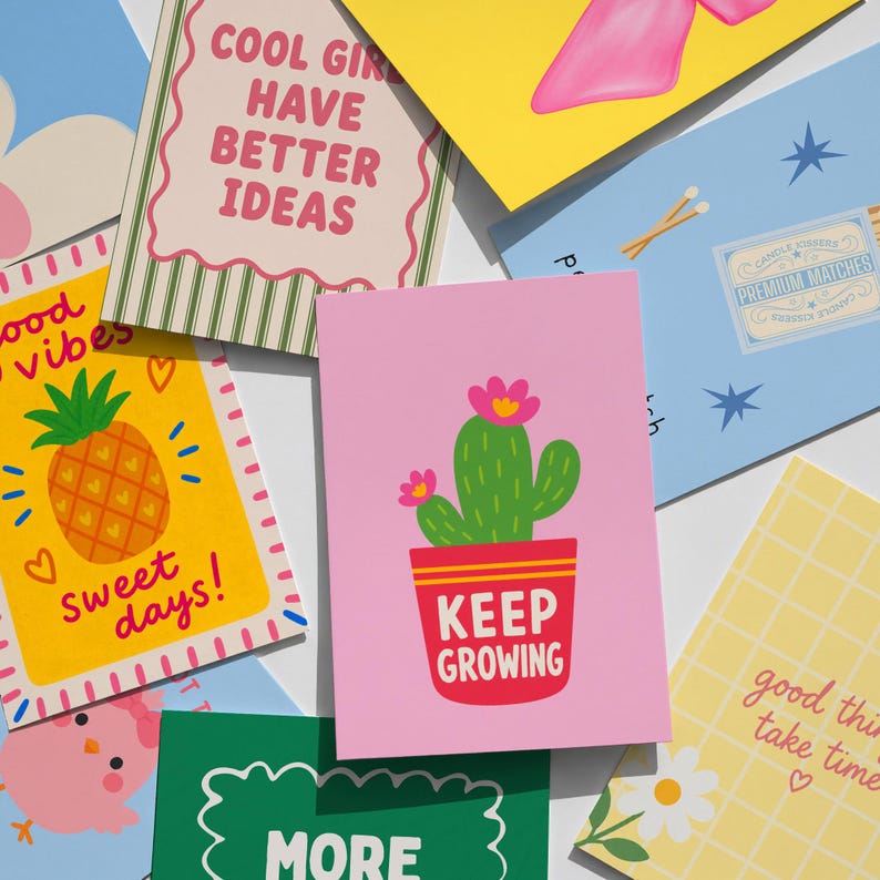 May include: A collection of colorful greeting cards featuring various illustrations and text. Designs include a green cactus in a red pot with the text KEEP GROWING, a yellow card with a pineapple and the text sweet days, and other cards with patterns, flowers, and phrases like COOL GIRL HAVE BETTER IDEAS.