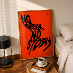K&ouml;nnte beinhalten: Gerahmtes Poster mit den schwarzen Worten "NO RISK NO STORY" auf leuchtend orangefarbenem Hintergrund. Das Poster befindet sich in einem goldenen Rahmen und wird in einem Raum mit Lampe, Kaffeetasse und Bett ausgestellt.