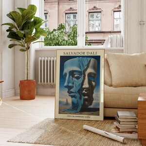 Op de afbeelding: Een poster met een surrealistisch schilderij van Salvador Dali. Het schilderij toont twee gezichten, waarvan er &eacute;&eacute;n gedeeltelijk bedekt is met een blauwe doek, met de tekst "Libera tus sentimientos ocultos" onderaan.