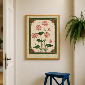May include: A rectangular framed wall art piece featuring a cream-colored background with a central illustration of pink lotus flowers and dark green leaves. The artwork is enclosed by a dark green border with small red floral accents and a light frame.