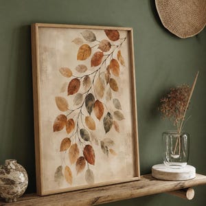 Op de afbeelding: Een rechthoekig ingelijst kunstwerk aan de muur met een botanische illustratie van een tak met talloze bladeren in tinten oranje, bruin, beige en gedempt groen tegen een getextureerde, lichtbeige achtergrond in een licht houten frame.