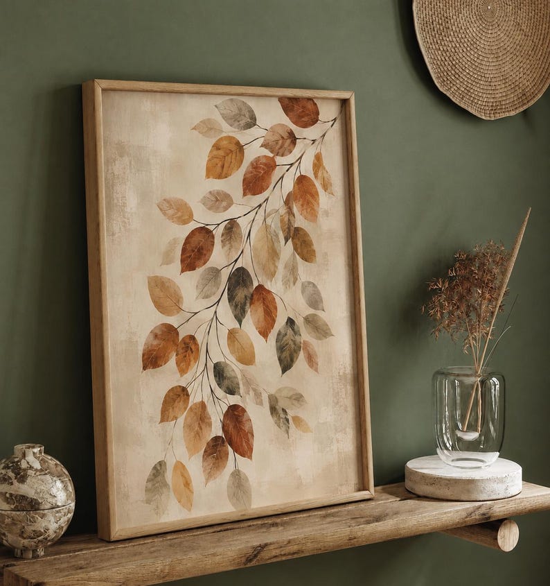 Op de afbeelding: Een rechthoekig ingelijst kunstwerk aan de muur met een botanische illustratie van een tak met talloze bladeren in tinten oranje, bruin, beige en gedempt groen tegen een getextureerde, lichtbeige achtergrond in een licht houten frame.