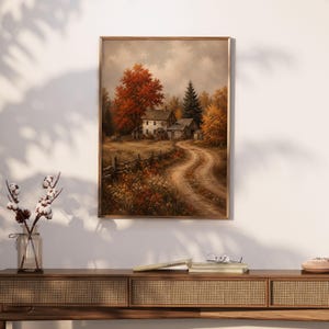 Op de afbeelding: Een ingelijste wandkunstprint met een landelijk landschap met een huis van twee verdiepingen, een kronkelend zandpad, een houten hek en herfstbomen met levendig oranje en geel gebladerte onder een bewolkte lucht.
