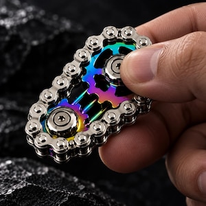 Pode incluir: Um brinquedo fidget spinner construído a partir de uma corrente de bicicleta metálica enrolada em torno de dois centros em forma de engrenagem com cores iridescentes de arco-íris. O dispositivo apresenta elos de metal prateado.