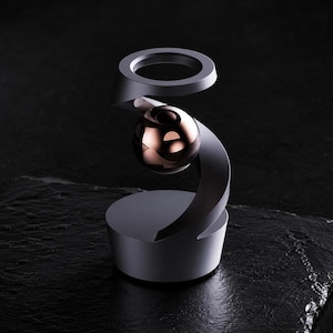 Peut inclure: Un support en métal gris foncé mat avec une structure en spirale qui soutient un objet sphérique en or rose poli suspendu au centre. La base est circulaire et solide, tandis que le sommet présente une ouverture en forme d'anneau au-dessus.