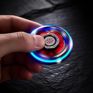 Op de afbeelding: Een ronde metalen fidget spinner met een felrood midden, een zilverkleurig metalen frame en een oplichtende blauwe LED-ring. De centrale dop toont een wit logo met de tekst MECHANICAL en andere kleine letters in een cirkelvormig patroon.
