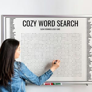 Könnte beinhalten: Ein weiß gerahmtes Wortsuchrätsel mit den Worten "COZY WORD SEARCH" oben. Das Rätsel wird mit einem schwarzen Marker bearbeitet. Die Worte "SLOW EVENINGS & SELF-CARE" stehen unter dem Titel. Eine Liste von Wörtern befindet sich auf den Seiten.