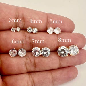 May include: A set of 6 pairs of gold stud earrings with clear round cubic zirconia stones. The earrings are shown in different sizes, from 3mm to 8mm.