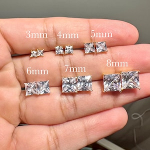 May include: A set of 10 pairs of square-shaped cubic zirconia stud earrings in gold settings. The earrings are displayed on a hand, with each pair labeled with its size in millimeters: 3mm, 4mm, 5mm, 6mm, 7mm, and 8mm.