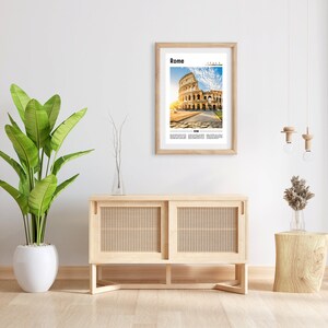May include: A framed print of the Colosseum in Rome, Italy. The print is in a light wood frame and is hanging on a white wall. There is a wooden cabinet with woven doors and a wooden stool with a vase of dried flowers on it.